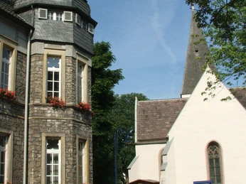 Rathaus Lage Historisches Rathaus mit Erker und blühenden Blumenkästen neben einer Kirche mit hohem Spitzdach.