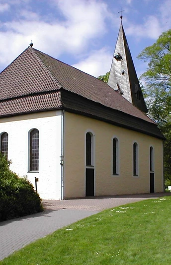 Kirche Stapelage Gelbe Kirche mit spitzem Turm, umgeben von Bäumen, auf einem gepflasterten Weg zugänglich.