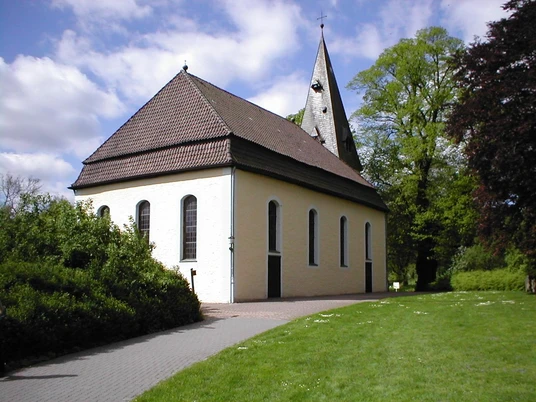Kirche Stapelage Gelbe Kirche mit spitzem Turm, umgeben von Bäumen, auf einem gepflasterten Weg zugänglich.