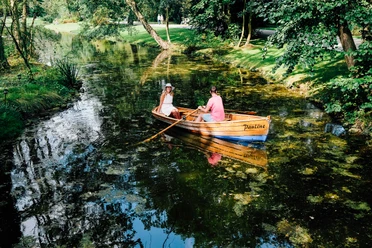 Rudern im Kurparksee im Landschaftsgarten Zwei Personen rudern in einem klassischen Holzboot auf einem von Bäumen gesäumten Kurparksee.