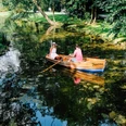 Rudern im Kurparksee im Landschaftsgarten Zwei Personen rudern in einem klassischen Holzboot auf einem von Bäumen gesäumten Kurparksee.