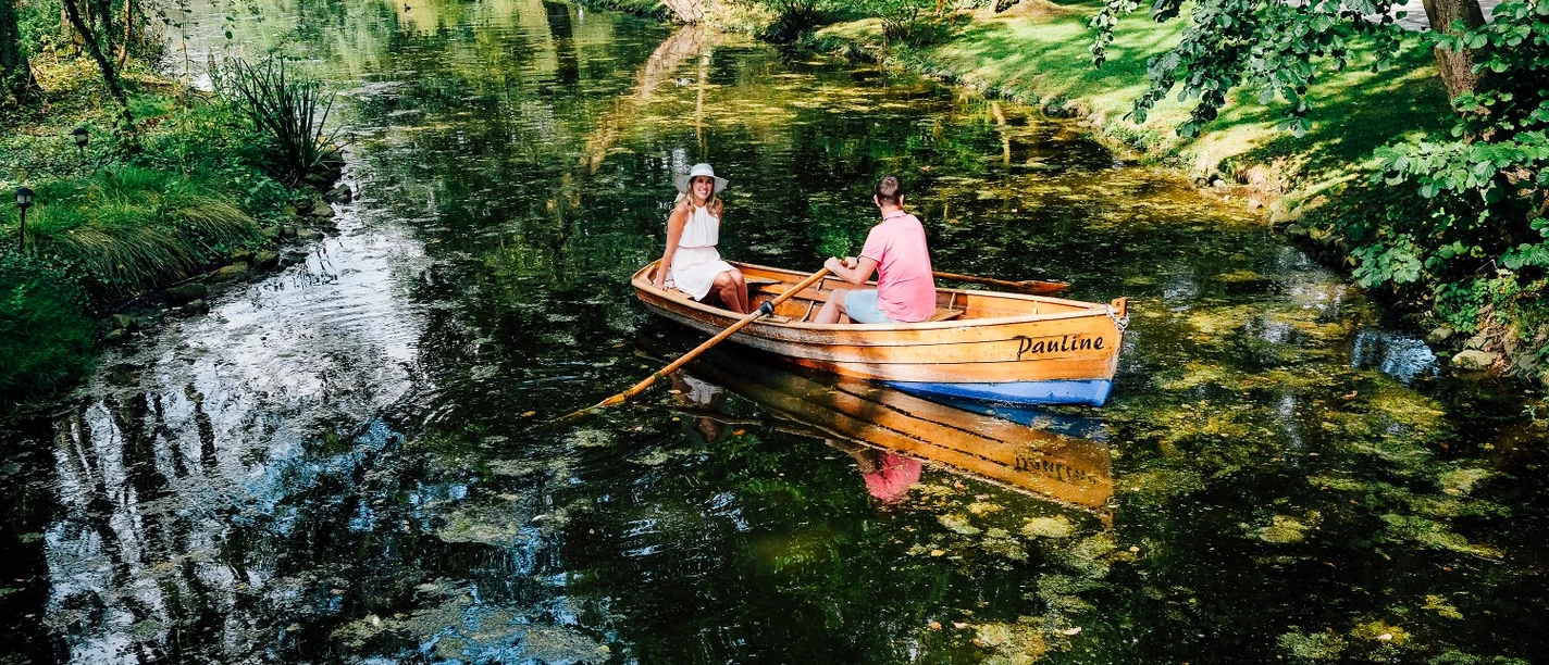 Rudern im Kurparksee im Landschaftsgarten Zwei Personen rudern in einem klassischen Holzboot auf einem von Bäumen gesäumten Kurparksee.