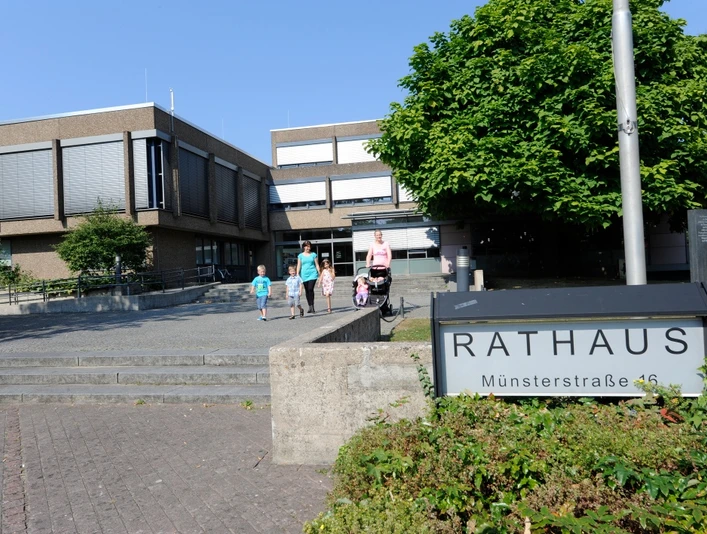 Rathaus Versmold Familie geht vor modernem Backsteingebäude zum Haupteingang des Rathauses mit grüner Umgebung.