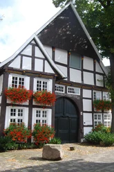 Historisches Fachwerkhaus mit blumengeschmückten Fenstern, großem Holztor und Kopfsteinpflaster davor.