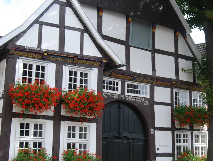 Historisches Fachwerkhaus mit blumengeschmückten Fenstern, großem Holztor und Kopfsteinpflaster davor.