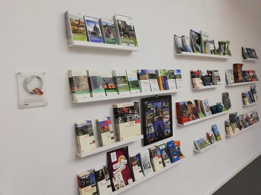Tourist-Information Lügde Faltblätter zu regionalen Sehenswürdigkeiten und Aktivitäten auf weißen Regalen an einer Wand.