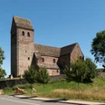 St. Kilianskirche in Lügde aus Bruchstein, umgeben von Bäumen; quadratischer Kirchturm, blauer Himmel.