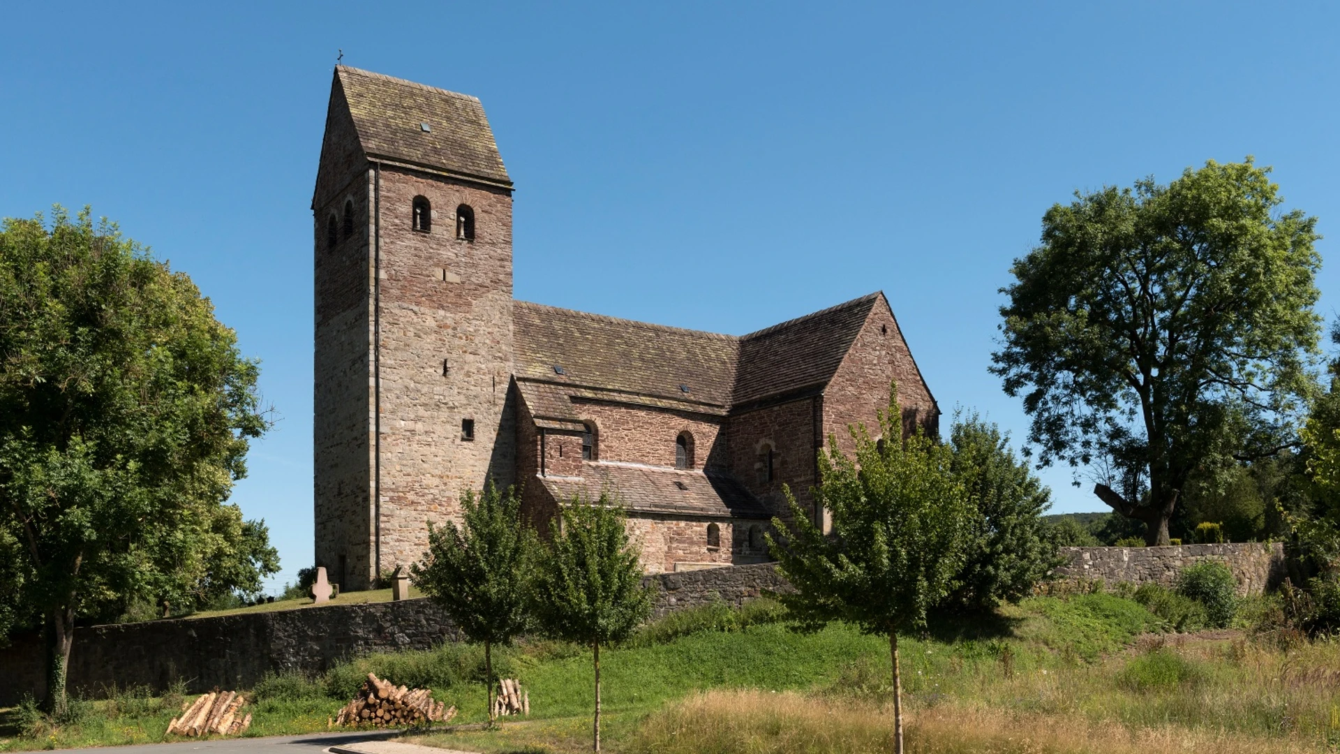 St. Kilianskirche in Lügde aus Bruchstein, umgeben von Bäumen; quadratischer Kirchturm, blauer Himmel.