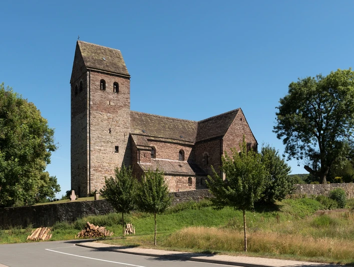 St. Kilianskirche in Lügde aus Bruchstein, umgeben von Bäumen; quadratischer Kirchturm, blauer Himmel.