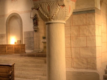 Eine romanische Kirche mit Lichtsäule und dekorativem Kapitell, helle Steinwände im Hintergrund.