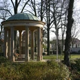 Pavillon im Park mit Säulen und Kuppeldach, umgeben von Bäumen und Landschaft im Winter.