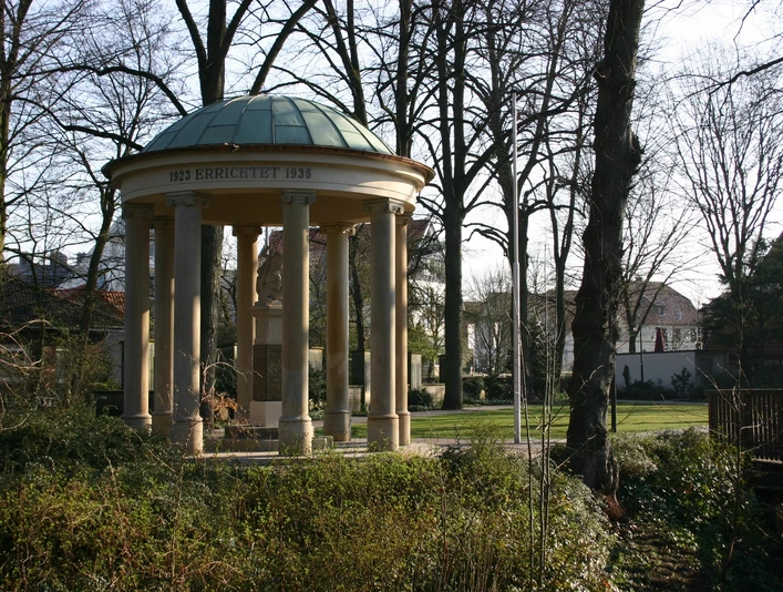 Kriegerdenkmal Pavillon im Park mit Säulen und Kuppeldach, umgeben von Bäumen und Landschaft im Winter.