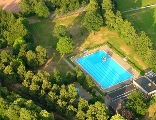 Ein Freibad mit einem großen, blauen Becken, umgeben von dichtem, grünem Waldgebiet.