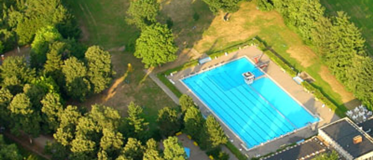 Ein Freibad mit einem großen, blauen Becken, umgeben von dichtem, grünem Waldgebiet.