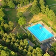 Freibad Rheda Ein Freibad mit einem groĂźen, blauen Becken, umgeben von dichtem, grĂĽnem Waldgebiet.