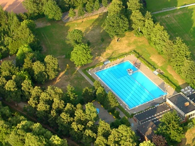 Freibad Rheda Ein Freibad mit einem großen, blauen Becken, umgeben von dichtem, grünem Waldgebiet.