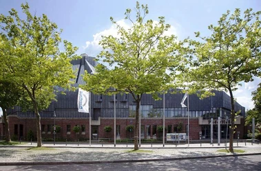 PaderHalle, Außenansicht Moderne Veranstaltungsstätte aus Backstein mit großem Eingangsbereich, umgeben von jungen Bäumen.
