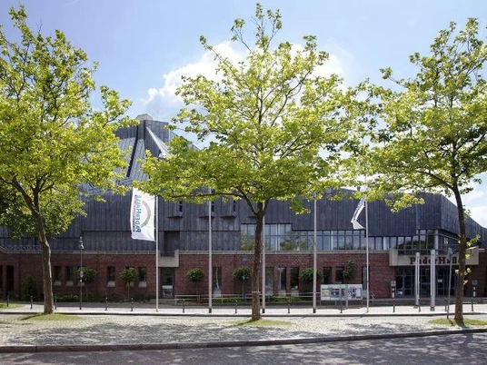 PaderHalle, Außenansicht Moderne Veranstaltungsstätte aus Backstein mit großem Eingangsbereich, umgeben von jungen Bäumen.