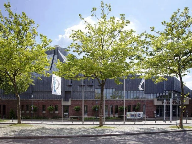 PaderHalle, Außenansicht Moderne Veranstaltungsstätte aus Backstein mit großem Eingangsbereich, umgeben von jungen Bäumen.