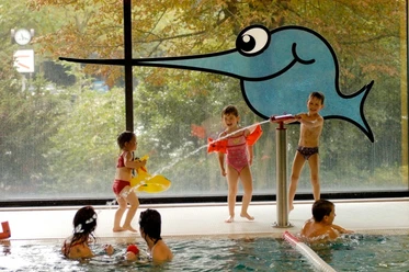 Schwimmoper - Kinderbecken Kinder spielen fröhlich im flachen Kinderbecken mit bunten Spielzeugen und lächeln einander an.