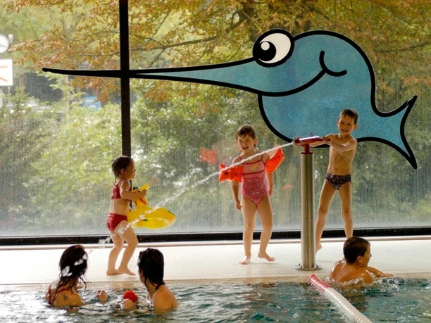 Schwimmoper - Kinderbecken Kinder spielen fröhlich im flachen Kinderbecken mit bunten Spielzeugen und lächeln einander an.