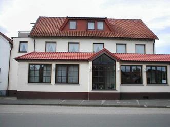 Traditionelles Gasthaus mit rotem Ziegeldach, weißen Wänden und großen Fenstern an einer Straße.