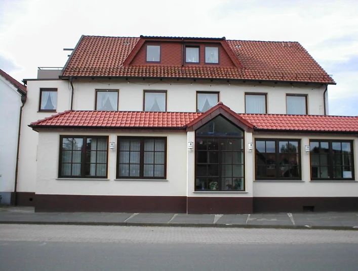 Hörster Krug Traditionelles Gasthaus mit rotem Ziegeldach, weißen Wänden und großen Fenstern an einer Straße.