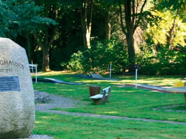 Minigolfanlage im Freizeitpark Eggetal Großer Gedenkstein in grüner Parkanlage mit Minigolfbahnen im Hintergrund, umgeben von Bäumen.
