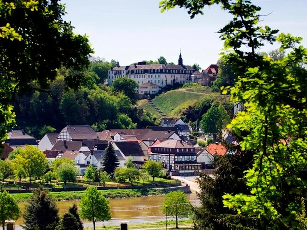 Abtei-vom-heiligen-kreuz-beverungen-herstelle-F-Grawe.jpg Blick auf die Abtei vom Heiligen Kreuz in Herstelle, umgeben von dichten Wäldern und einem Fluss.