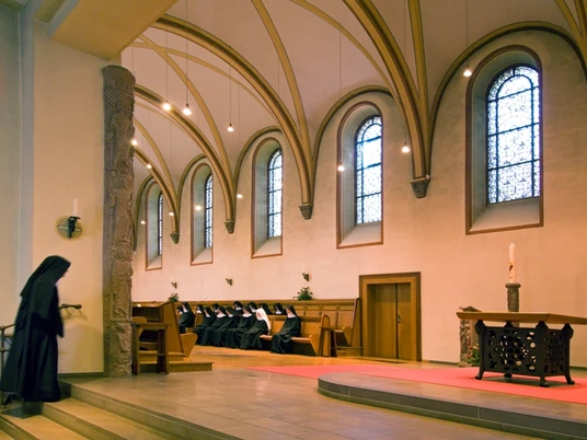 Betende Nonnen in einer Abtei mit gotischen Fenstern und einem beeindruckenden geschnitzten Altar.