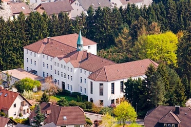 Dreifaltigkeitskloster Bad Driburg Luftaufnahme des weißen Dreifaltigkeitsklosters, umgeben von dichtem Wald und Wohnhäusern.