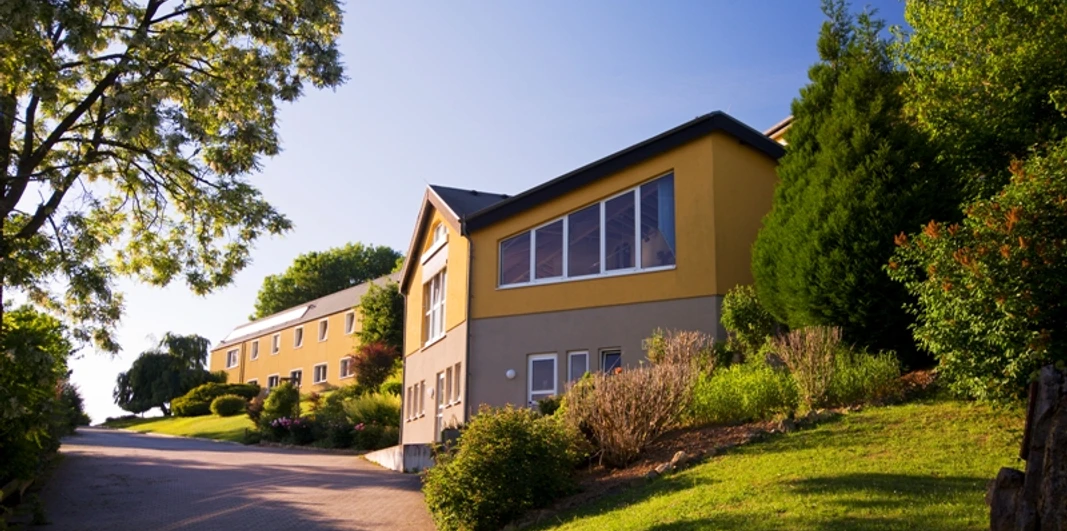 Diakonissen-Kommunität Zionsberg in Warburg-Scherfede Gelbes Gebäude mit vielen Fenstern auf einem grünen Hügel, umgeben von Bäumen und Sträuchern.