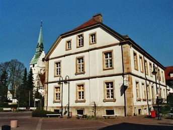 Ehemaliges Bürgermeisterhaus Ein historisches Gebäude mit Fachwerkflair vor einem Kirchturm, umgeben von Bäumen und blauem Himmel.