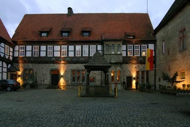 Burghof Historischer Burghof mit altem Brunnen, umgeben von Fachwerkgebäuden, in abendlicher Beleuchtung.