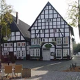 Fachwerkhaus am Kopfsteinpflasterplatz mit Terrasse, herbstlichen Bäumen und Sitzgelegenheiten.