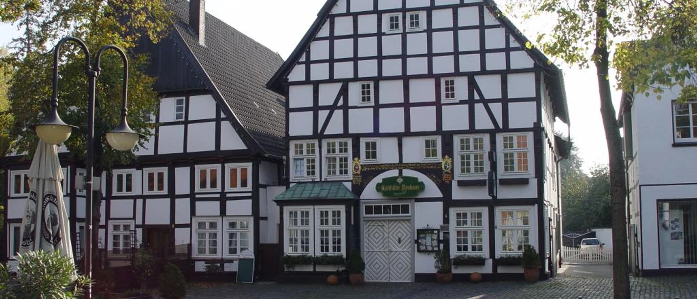 Fachwerkhaus am Kopfsteinpflasterplatz mit Terrasse, herbstlichen Bäumen und Sitzgelegenheiten.