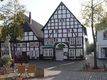Fachwerkhaus am Kopfsteinpflasterplatz mit Terrasse, herbstlichen Bäumen und Sitzgelegenheiten.