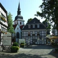 Fachwerkhäuser und Kirche in einer historischen Altstadt mit sonnigem Platz und Café-Tischen.