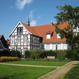 Drostenhaus und Drostegarten Historisches Fachwerkhaus mit Garten und roten Ziegeldächern, vor blauem Himmel und grünen Büschen.