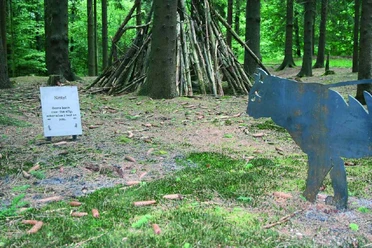 Kitty come back Ein hölzernes Kunstwerk im Wald mit Katzenfigur und einem Infobord, umgeben von Bäumen.
