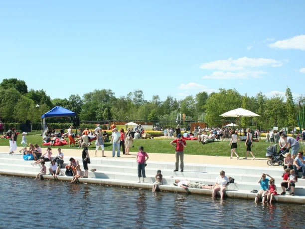 Entspannung am Untersee Menschen entspannen sich an einem sonnigen Tag am Ufer eines Flusses in einem belebten Park.