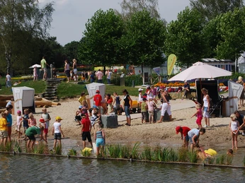 Sandstrand am Obersee Familien und Kinder spielen und entspannen am sandigen Ufer eines Sees mit üppigem Grün im Hintergrund.