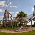 Moderne Spielplatzstruktur aus Metall mit Röhrenrutschen und Kletterelementen in einem Park.