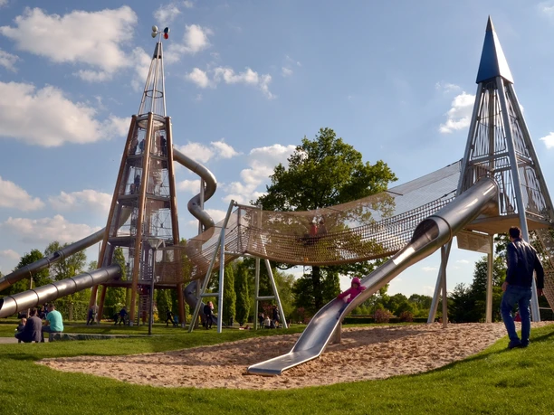 Das Wahrzeichen im Parkteil Nord - der Rutschenturm Moderne Spielplatzstruktur aus Metall mit Röhrenrutschen und Kletterelementen in einem Park.