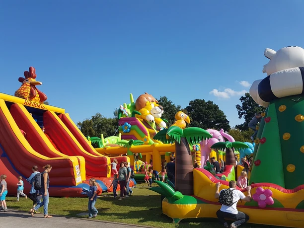 Kinder und Erwachsene genießen eine bunte Hüpfburg-Anlage mit Tiermotiven bei sonnigem Wetter.