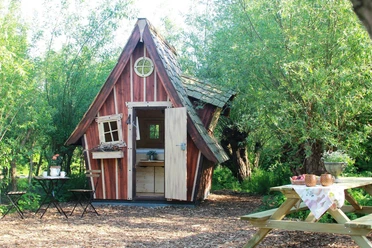 Kleines Hexenhäuschen aus Holz im Grünen mit offener Tür und Picknickbank