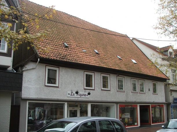 Frontalansicht eines zweistöckigen Gebäudes mit Schaufenstern im Erdgeschoss und einem Ziegeldach.