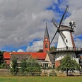 Klostermühle Lahde Historische Windmühle neben einer Kirche, umgeben von Bäumen und einem leichten Wolkenhimmel.