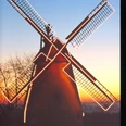 Valentins Mühle Eine historische Windmühle bei Sonnenuntergang, beleuchtet von Lichterketten mit Bäumen im Hintergrund.