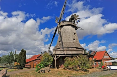 Meßlinger Mühle 2 Historische Windmühle mit grauen Schindeln, Holzgalerie und Flügeln vor blauem Himmel und Wolken.